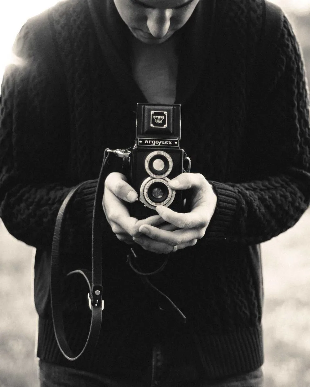 Creator holding a twin-lens camera up to the lens, black and white