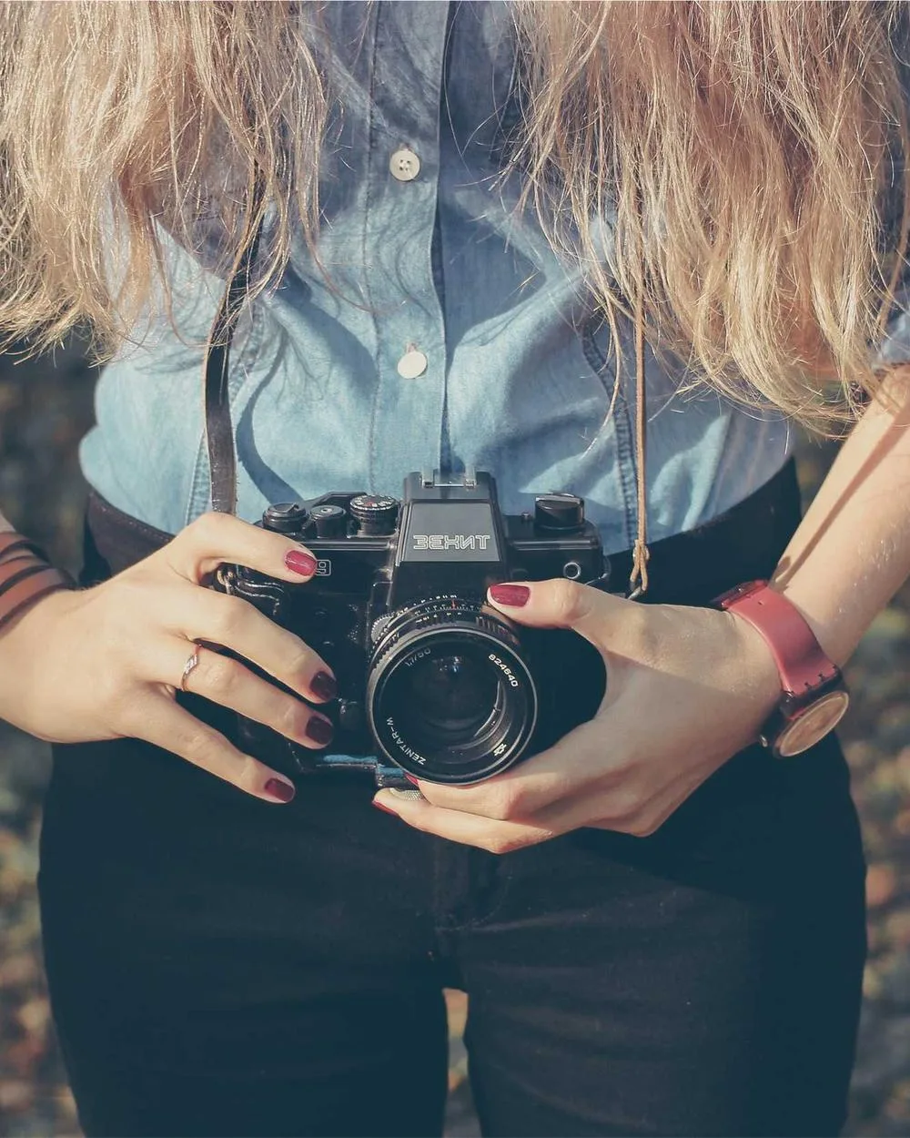 Creator in a denim shirt holding a mirrorless camera at chest height