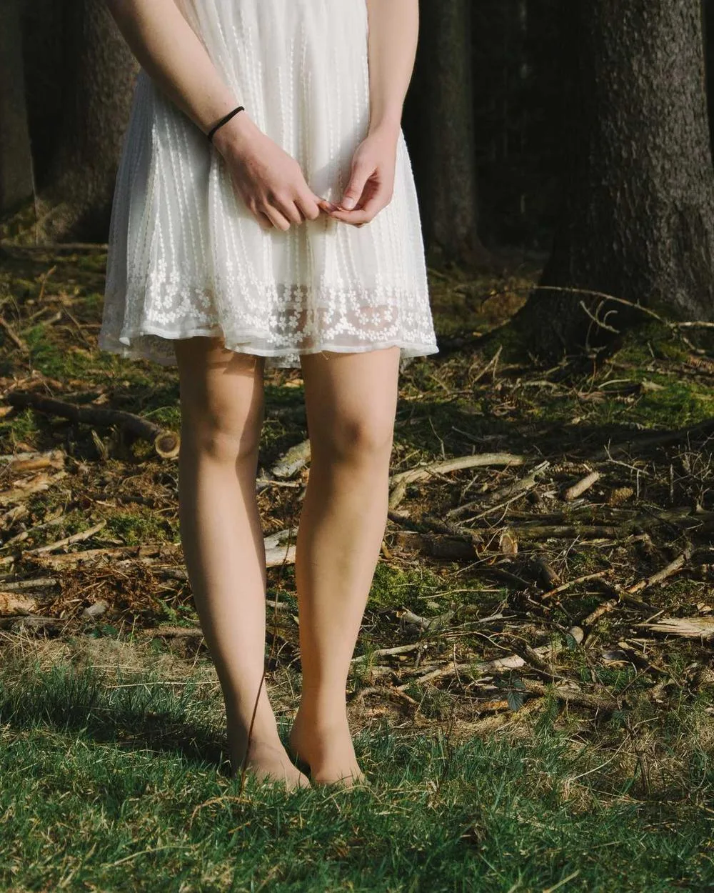 Creator in a white dress standing barefoot on grass, cropped at the shoulders