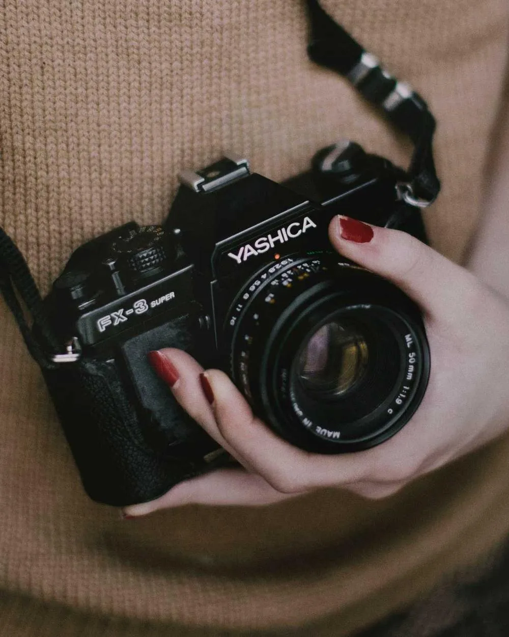 Hands holding a vintage film camera against a woollen sweater