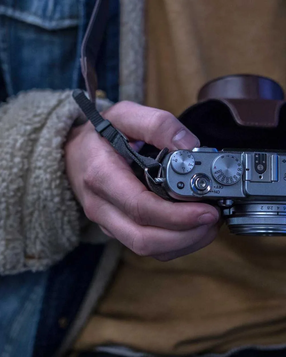 Creator holding a rangefinder camera, cropped to the hands and jacket