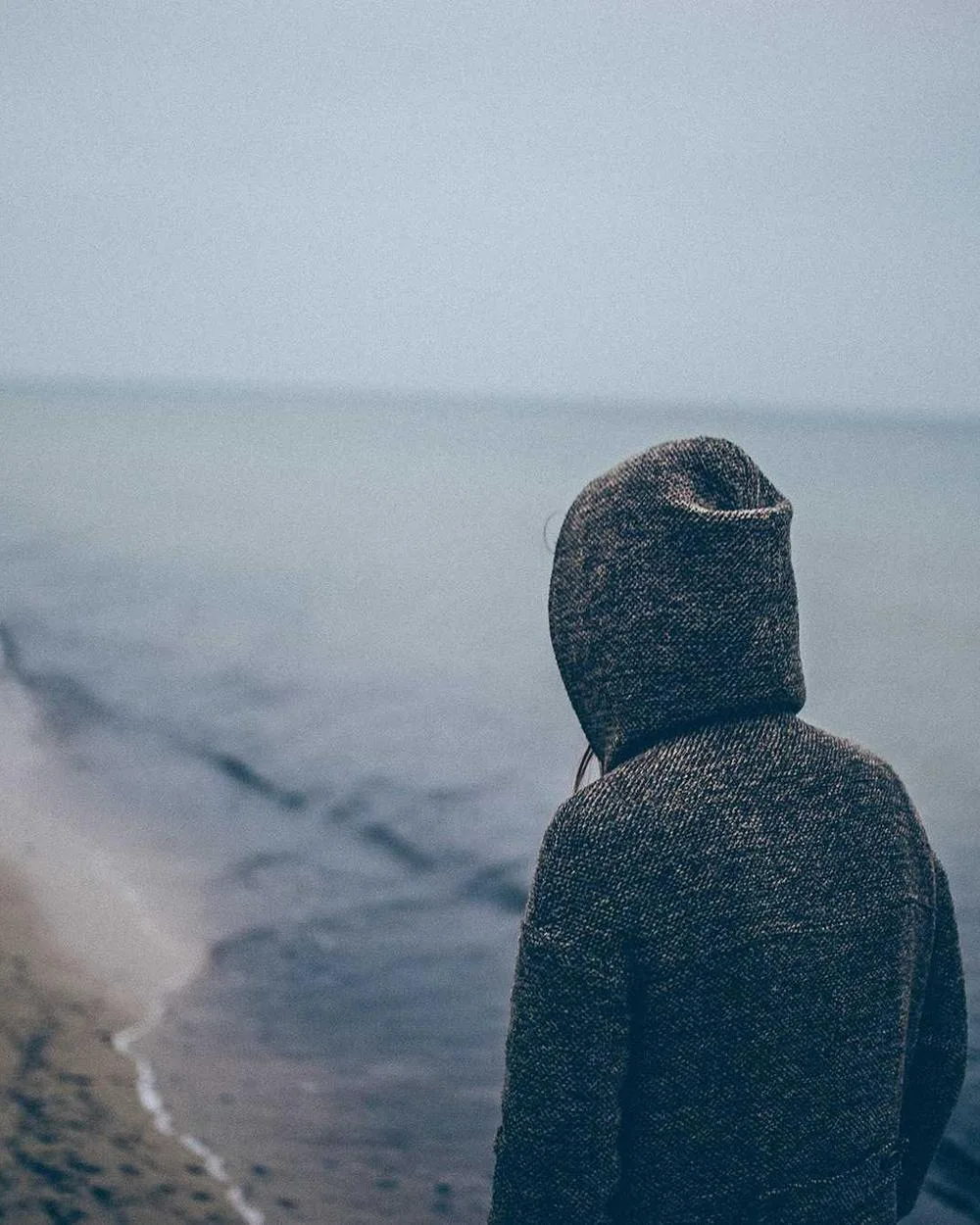 Creator in a hoodie facing the sea from a beach