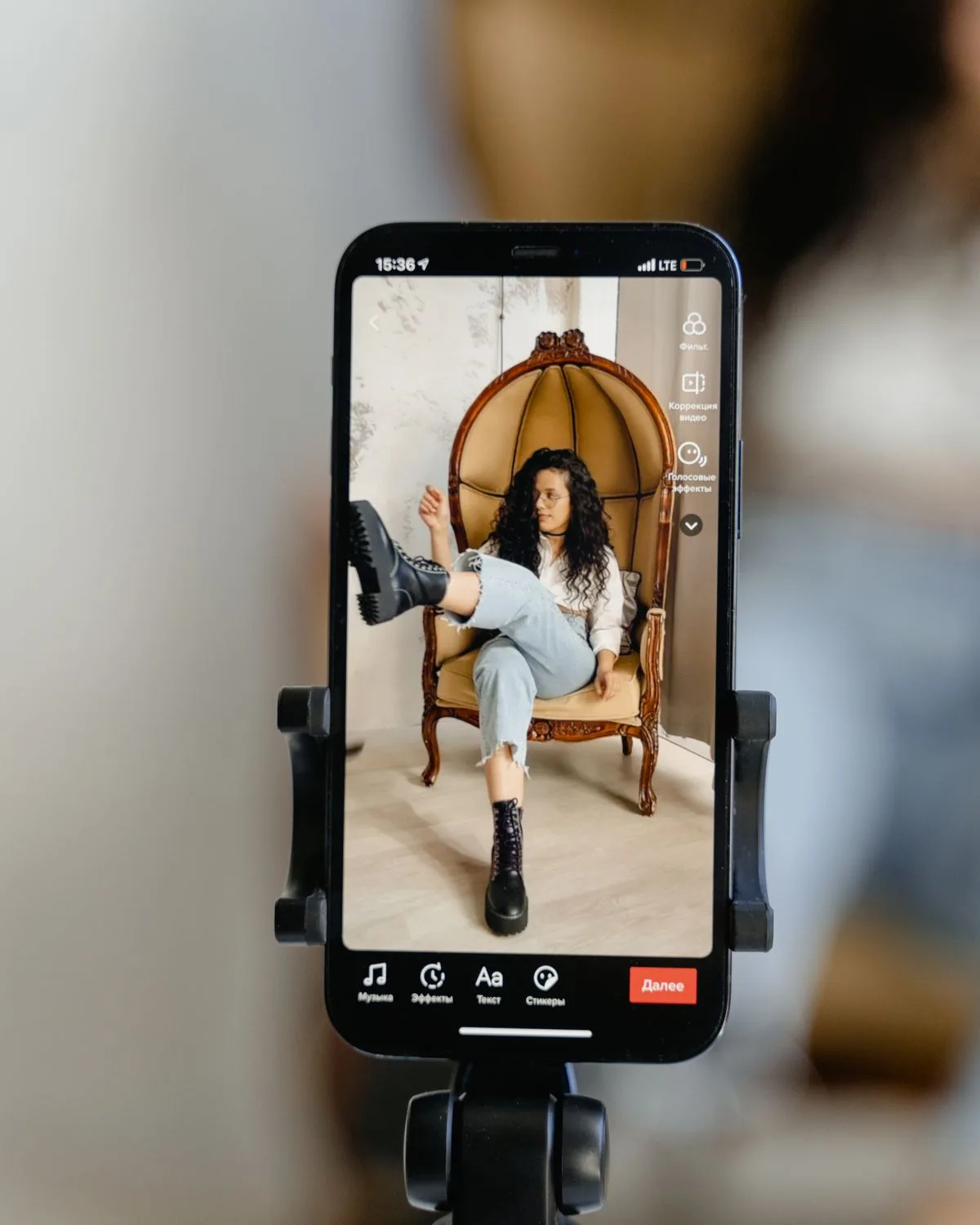 Phone on a tripod framing a creator seated in a wicker chair, mid-recording