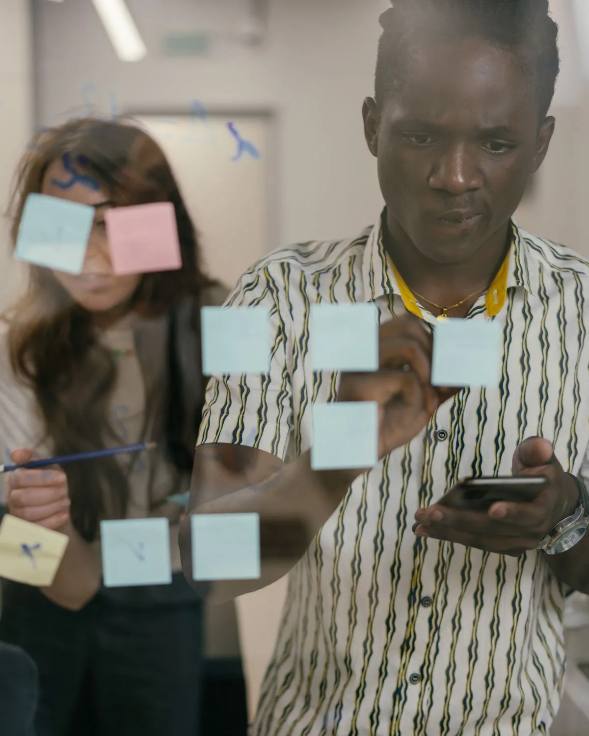 Two colleagues planning with sticky notes on a glass wall